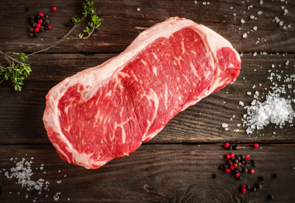 100% grass-fed New York Strip steak on a wooden surface with salt and peppercorns